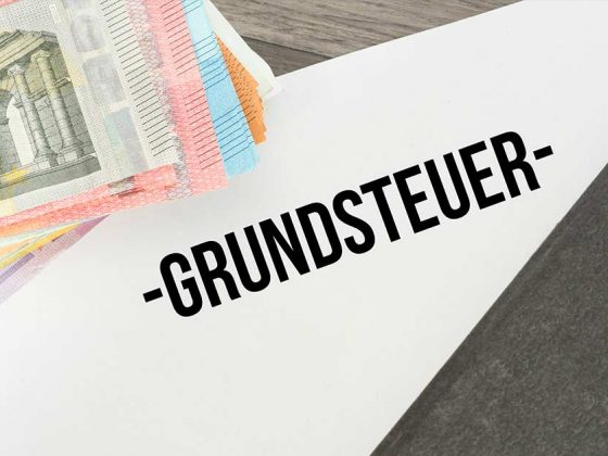 Auf einem Schreibtisch liegen Geldscheine, ein Ordner und ein Papier mit dem Wort "Grundsteuer" - Grundsteuer