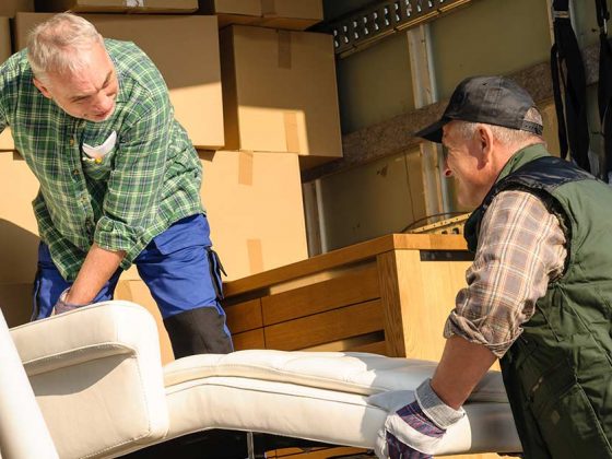 Zwei Männer heben in einem Umzugswagen voller Kisten ein Sofa an - Wohnen im Alter