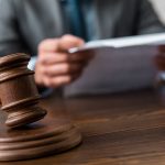 Ein Richterhammer auf einem Schreibtisch und zwe Hände, die Papiere halten - Gesetze, die ein Makler kennen muss