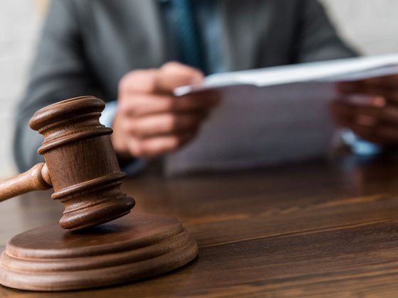 Ein Richterhammer auf einem Schreibtisch und zwe Hände, die Papiere halten - Gesetze, die ein Makler kennen muss