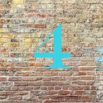 Die Zahl Vier in blau vor einer braun-roten Backsteinwand - Kleine Wohnfläche