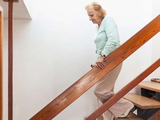 Alte Dame geht eine Holztreppe in ihrem Einfamilienhaus herunter.