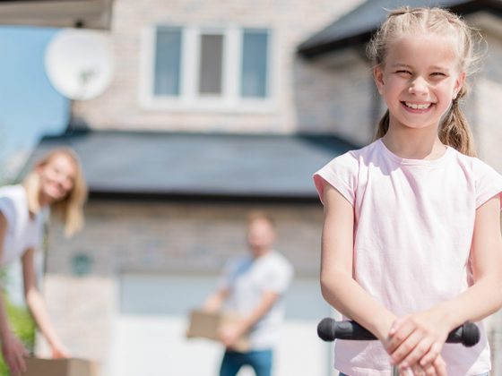 Ein Mädchen vor einem Haus, im Hintergrund die Eltern - Immobilienverkauf