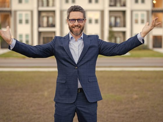 Ein Verwalter in witziger Pose vor einem Mehrfamilienhaus