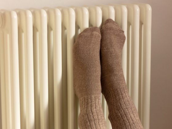 Jemand presst vor Kälte seine Füße mit Socken an eine Heizung, um nicht zu frieren